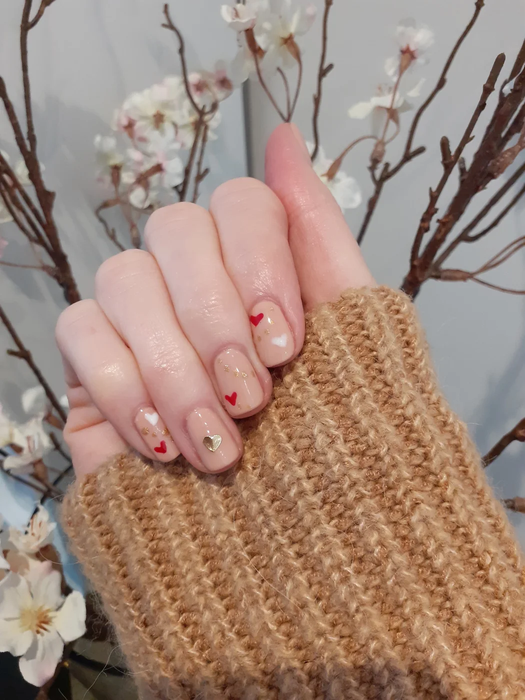 A finished manicure with small red and gold heart nail art